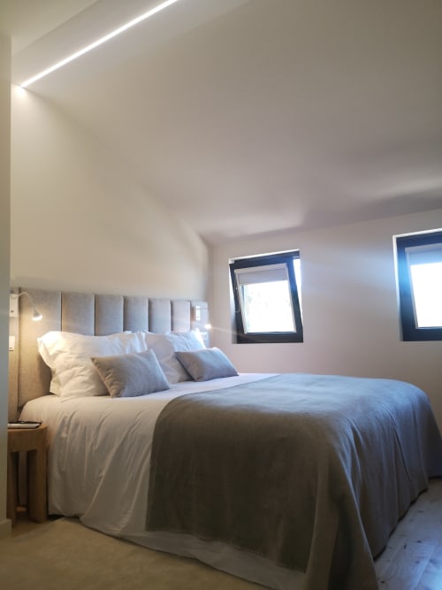 Quarto moderno da quinta Em Xisto na serra de Góis, Portugal, com cabeceira acolchoada, detalhes em azul e luz natural das janelas