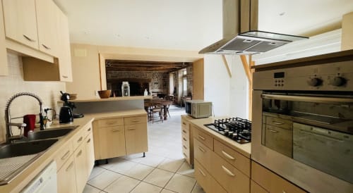 Spacieuse cuisine du cottage de Corrèze avec armoires crème, cuisinière à gaz et appareils modernes donnant sur la salle à manger