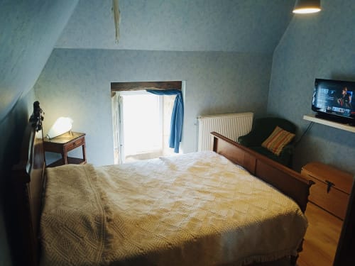Chambre douillette dans le cottage de Corrèze avec lit en bois, bureau, portes vitrées sur le jardin et TV sur radiateur