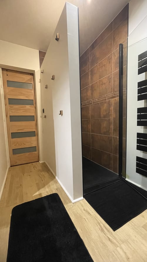 Couloir de salle de bain moderne avec douche en carrelage marron, porte en bois et tapis noirs au gîte Conciergerie Pour Tous