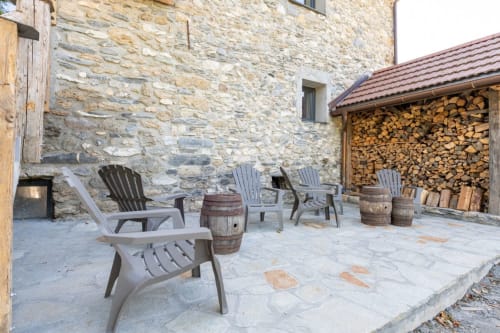 Patio en pierre avec chaises Adirondack, tables tonneau et bois de chauffage empilé à Domaine de l'Epigny