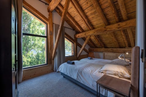 Chambre chaleureuse avec poutres apparentes, vue montagne, grandes fenêtres et literie blanche au Domaine de