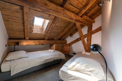 Chambre de chalet rustique aux poutres apparentes, deux lits en lin blanc, puits de lumière et vue sur les montagnes au Domaine de