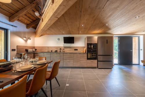 Cuisine-séjour contemporaine avec poutres en bois, vue sur les montagnes et électroménagers en acier inoxydable aux Alpes françaises