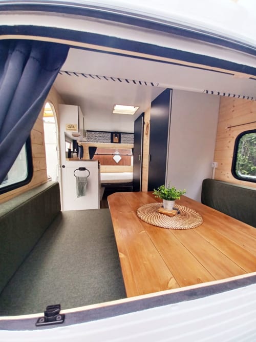 Intérieur de camping-car moderne avec table en bois, coin salon, kitchenette et chambre au gîte La Cour d'Hortense