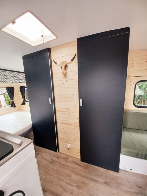 Intérieur moderne de camping-car avec portes coulissantes noires, lambris bois et puits de lumière au gîte La Cour d'Hortense