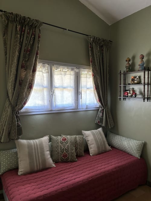 Cozy bedroom nook at Domaine Du Commandeur with red daybed, sage green walls, patterned curtains and garden view window in