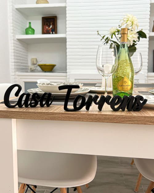 Mesa de comedor Casa Torrens con botella de vino Sandara, copas, margaritas blancas y letrero en script negro en Polop de la Marina