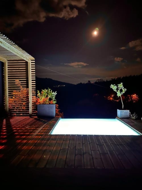 Piscina externa iluminada em deck de madeira na quinta Em Xisto em Góis, Portugal, com vista para colinas florestadas