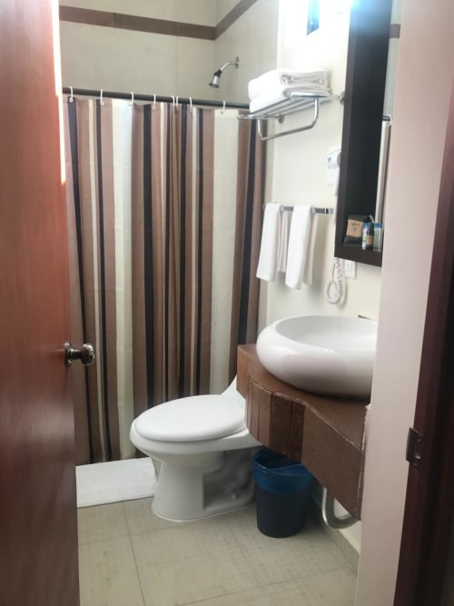 Baño del Hotel El Candelero en Yuriria con inodoro, lavabo redondo, cortina de ducha a rayas y toallero