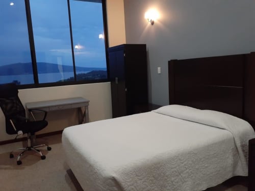 Habitación moderna del Hotel El Candelero en Yuriria con cama blanca, muebles de madera oscura, área de trabajo y vistas al lago al atardecer