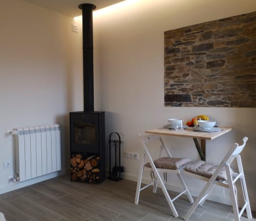 Interior da villa moderna em Em Xisto com fogão de madeira preta, radiador branco, mesa de jantar e parede de pedra em Góis