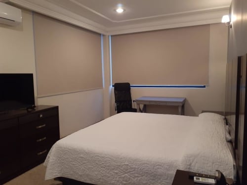 Dormitorio moderno del Hotel El Candelero en Yuriria con cama queen, escritorio, muebles de madera oscura y cortinas motorizadas.