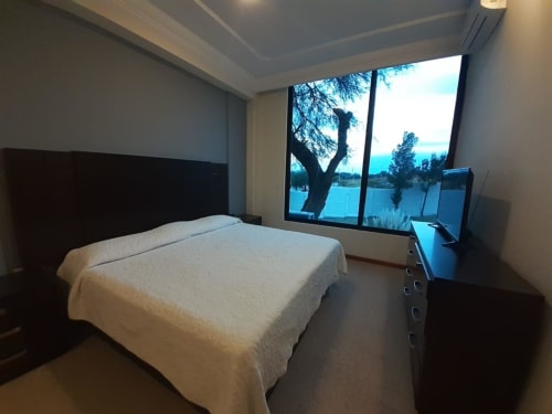 Habitación moderna en Hotel El Candelero de Yuriria con vista a la piscina, cama blanca, cabecero oscuro y amplios ventanales