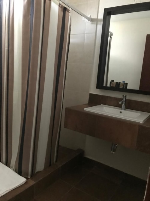 Baño moderno del Hotel El Candelero en Yuriria con lavabo, espejo y cortina de ducha a rayas