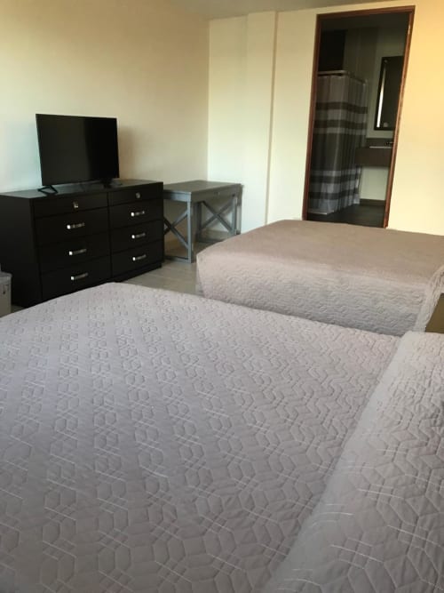 Habitación del Hotel El Candelero en Yuriria con dos camas, televisor, cómoda negra y entrada al baño