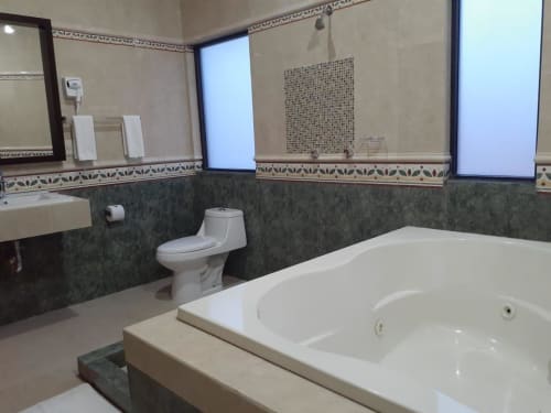 Baño espacioso del Hotel El Candelero en Yuriria con bañera blanca, inodoro blanco, dos lavabos y azulejos decorativos