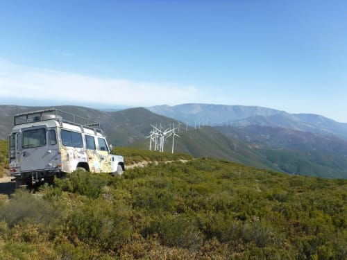 Autocaravana estacionada na encosta perto de Em Xisto em Góis, Portugal, com aerogeradores e montanhas ao fundo