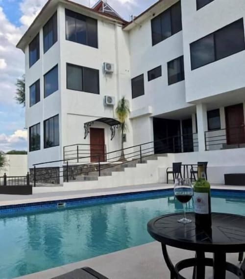 Área de piscina del Hotel El Candelero con edificio blanco moderno, agua turquesa y copa de vino en Yuriria, México