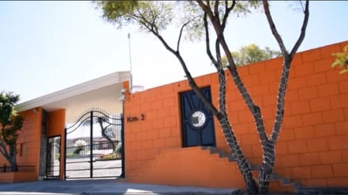 Entrada del Hotel El Candelero en Yuriria con fachada de ladrillo naranja, puerta metálica y árboles desérticos