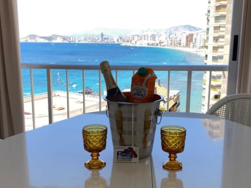 Balcony celebration at Benidorm beachfront apartment with champagne, glasses, and sea view overlooking Benidorm coast