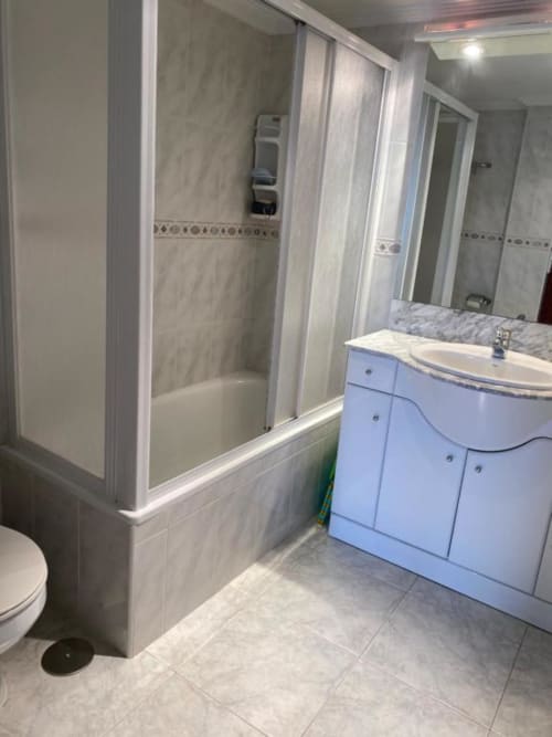 Modern bathroom in Benidorm apartment with blue vanity, shower enclosure, marble-style tiling, and toilet