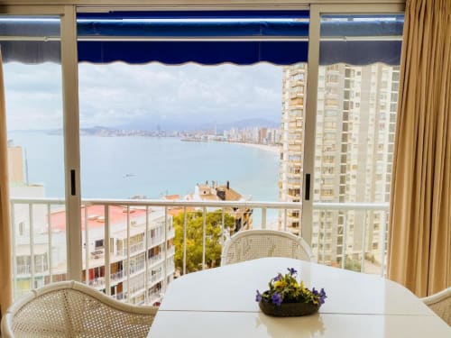 Bright Benidorm apartment balcony with sea views of Mediterranean coast, modern dining table, and coastal cityscape