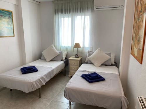 Twin bedroom with sea view at Tads Holiday Lets in Benidorm, featuring two single beds, nightstand, lamp, and large windows