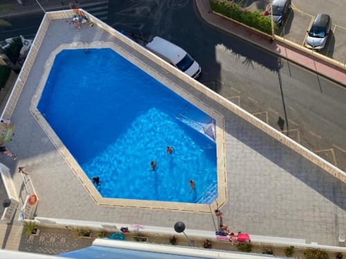 Aerial view of Tads Holiday Lets pool in Benidorm with guests swimming, surrounded by deck area and parked cars