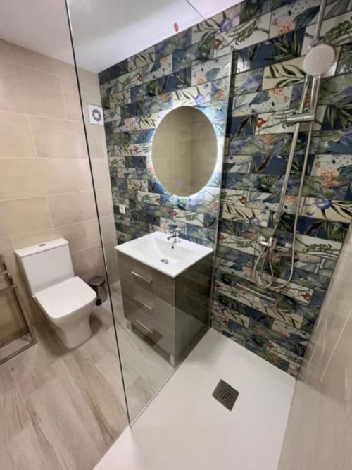 Modern bathroom at Lidersol Apartments, Benidorm with botanical tiled walls, illuminated oval mirror, white sink vanity, and