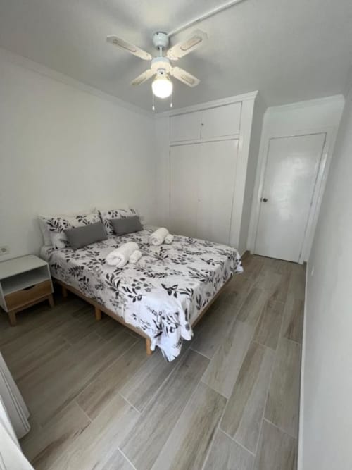 Bright bedroom with queen bed, floral bedding, ceiling fan, white wardrobe, tile flooring at Lidersol Apartments, Benidorm