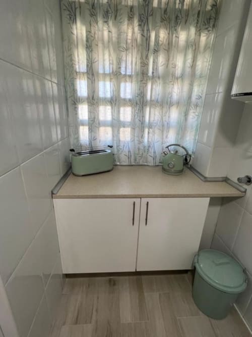 Compact bathroom in Lidersol Apartments, Benidorm with white cabinetry, sage green toilet and kettle, patterned curtains, and