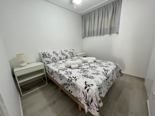 Modern bedroom in Lidersol Apartments, Benidorm with floral bedding, nightstand, lamp, and city view window with curtains