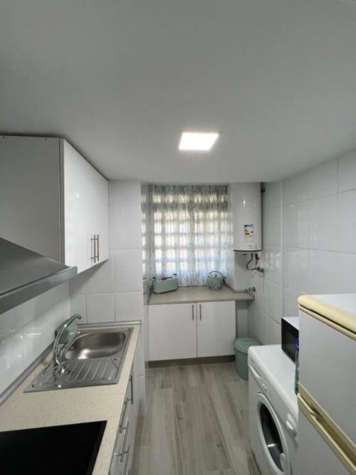 Modern kitchen in Lidersol Apartments, Benidorm with white cabinets, sink, microwave, washing machine and window