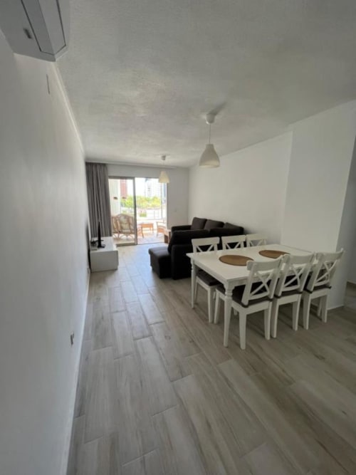 Modern apartment in Benidorm with white dining table, black sofa, wooden flooring, and balcony view at Lidersol Apartments