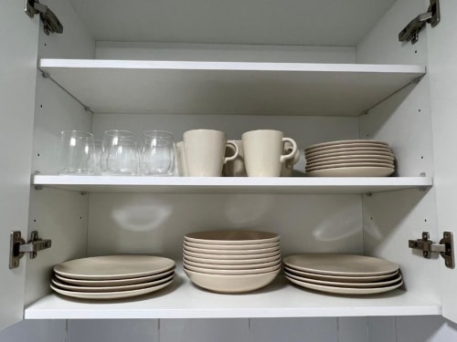 White kitchen cabinet with organized dishware including glasses, mugs, plates and bowls at Lidersol Apartments, Benidorm.