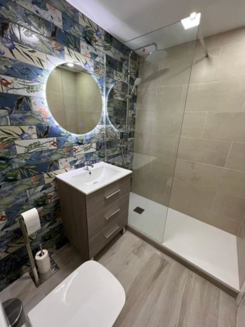 Modern bathroom in Lidersol Apartments, Benidorm with floral feature wall, lit mirror, white sink and shower enclosure