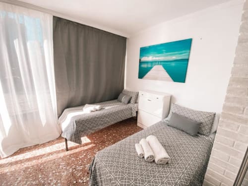 Bright twin bedroom in Lidersol Apartments, Benidorm with grey patterned bedding, turquoise ocean pier artwork, and modern