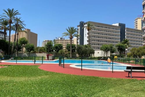 Benidorm apartment complex with swimming pool, red sports court, green lawn, palm trees and modern residential buildings