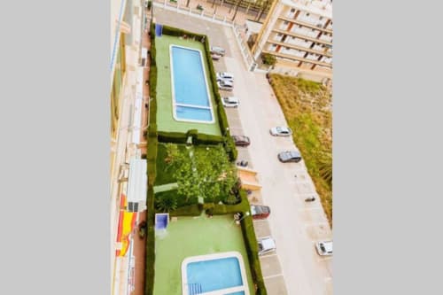 Aerial view of Mariscal Apartments pool area in Benidorm with two blue pools, green gardens, and parking spaces surrounded by
