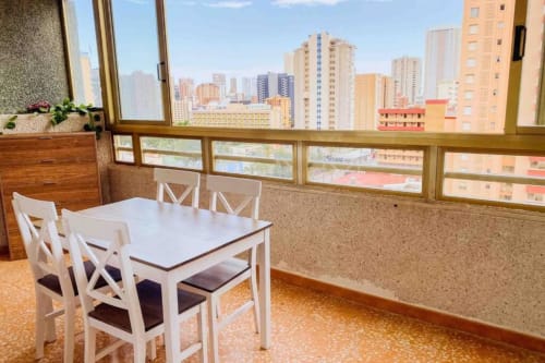 Dining area with white table and chairs overlooking Benidorm cityscape from high-rise apartment balcony