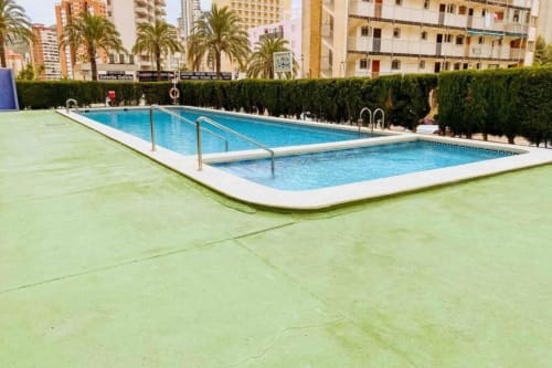 Twin swimming pools with blue water at Mariscal Apartments in Benidorm, surrounded by palm trees and residential buildings