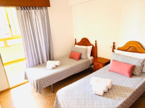 Twin bedroom with wooden beds, coral pillows, and white towels at Mariscal Apartments in Benidorm