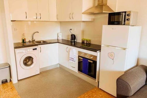 Modern kitchen in Mariscal Apartments, Benidorm with white cabinets, black countertops, washing machine, oven, and stainless
