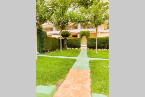 Lush courtyard garden at Mariscal Apartments in Benidorm with manicured lawns, mature trees, and terracotta pathway leading