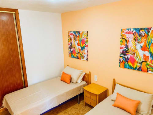 Bright bedroom at Tads Holiday Lets in Benidorm with two beds, orange accents, colorful tropical artwork, and yellow