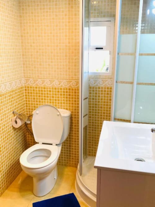 Bright yellow tiled bathroom with white toilet, shower cubicle, and sink in Zafiro Apartments, Benidorm