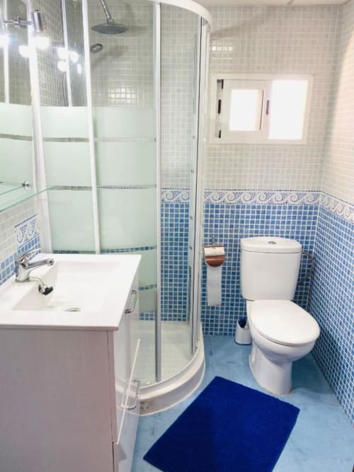 Modern bathroom at Tads Holiday Lets in Benidorm with blue mosaic tiles, white sink, toilet, and curved shower enclosure