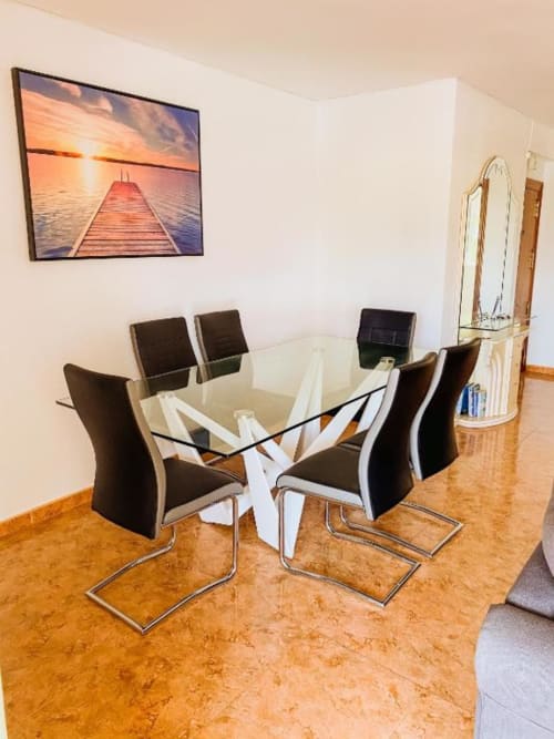 Modern dining area at Zafiro Apartments in Benidorm with glass table, black chairs, and sunset pier artwork on white walls