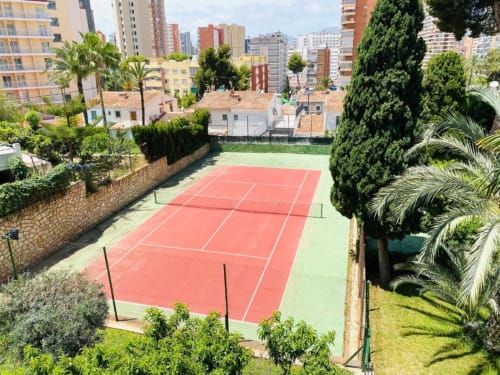Tennis court in lush garden at Zafiro Apartments, Benidorm, surrounded by palm trees and apartment buildings